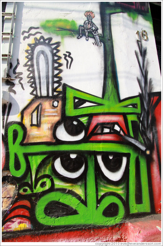 Graffiti: many green noses, a few eyes, a couple mouths, a cigarrette, a chainsaw, and a person sawing off the tree branch he's sitting on with a handsaw.  Villa Magdalenda neighborhood.  Rua Belmiro Braga and Rua Cardeal Arcoverde.