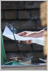 Hand holding a paper behind burning incense. Tana Baru cemetery, Bo-Kaap.